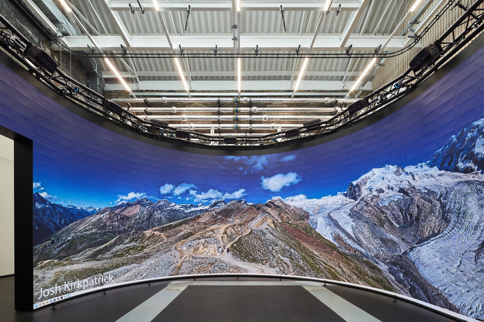 The curved panoramic screen of the Reality Emulator, showing a mountain and glacier panorama, credited to Josh Kirkpatrick.